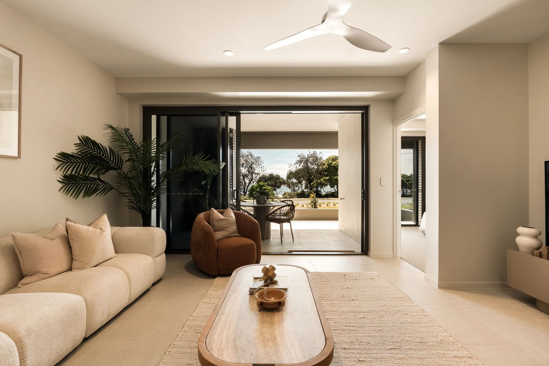 Living room of the completed residence, the sofa and travertine coffee table facing wide open sliding doors to the terrace, the Esplanade and the sea