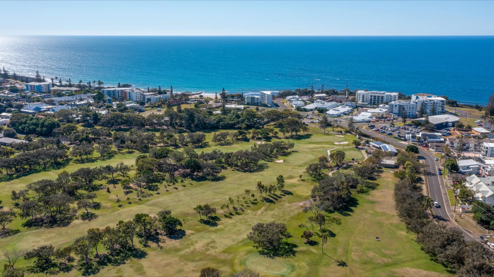 Aerial view over Bargara — the golf course and township in the foreground, the Esplanade apartments and the Coral Sea beyond