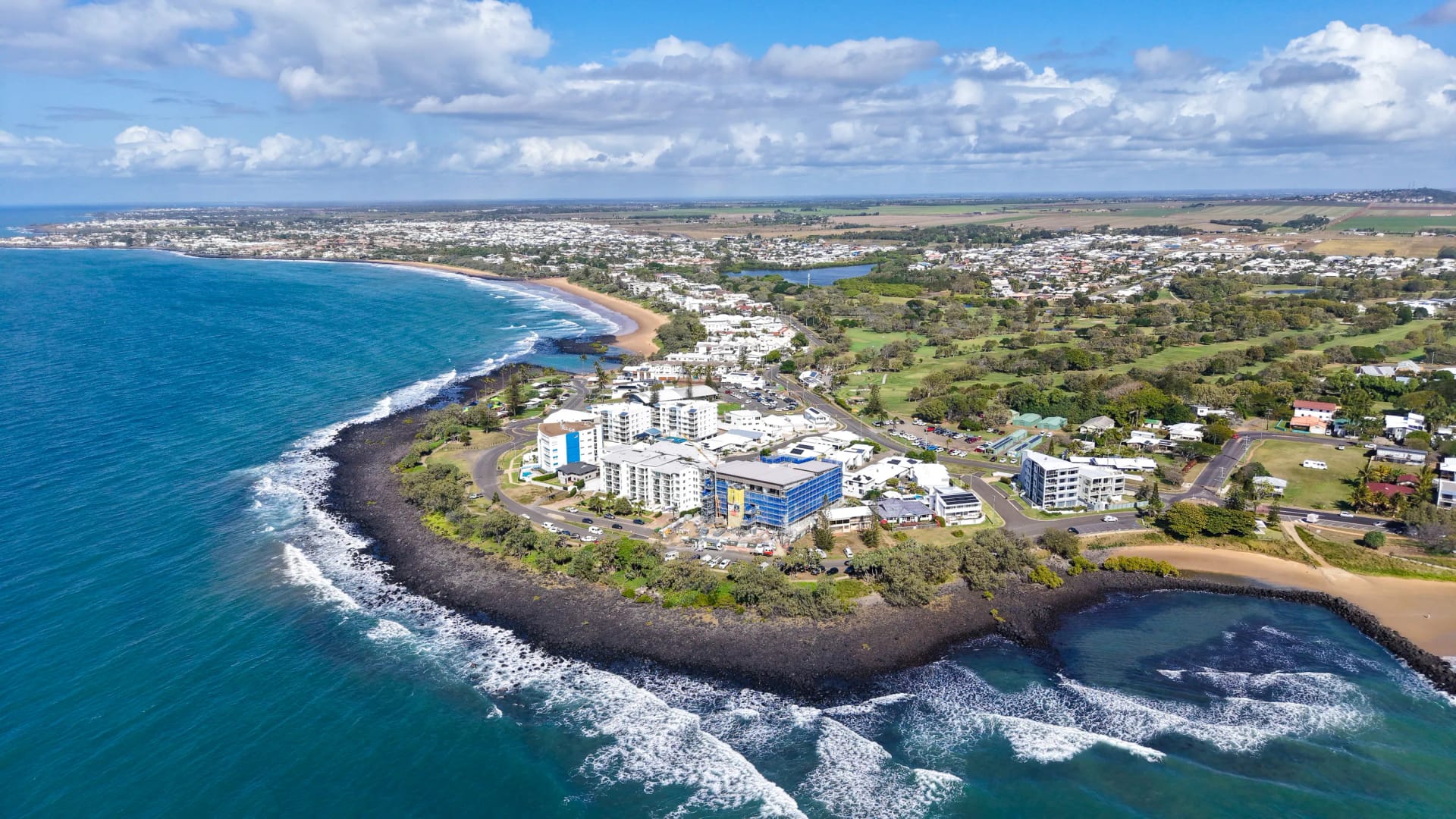 Aerial photograph of the Bargara headland, its rock shelf and beaches, with the township and golf course behind