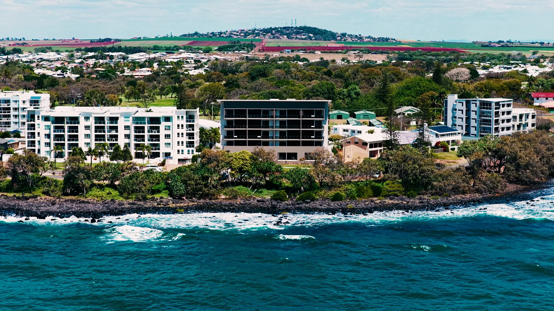 Aerial photograph of the completed Mira Living on the Bargara Esplanade, the rock shelf and beach in front of it and the township, golf course and cane fields behind