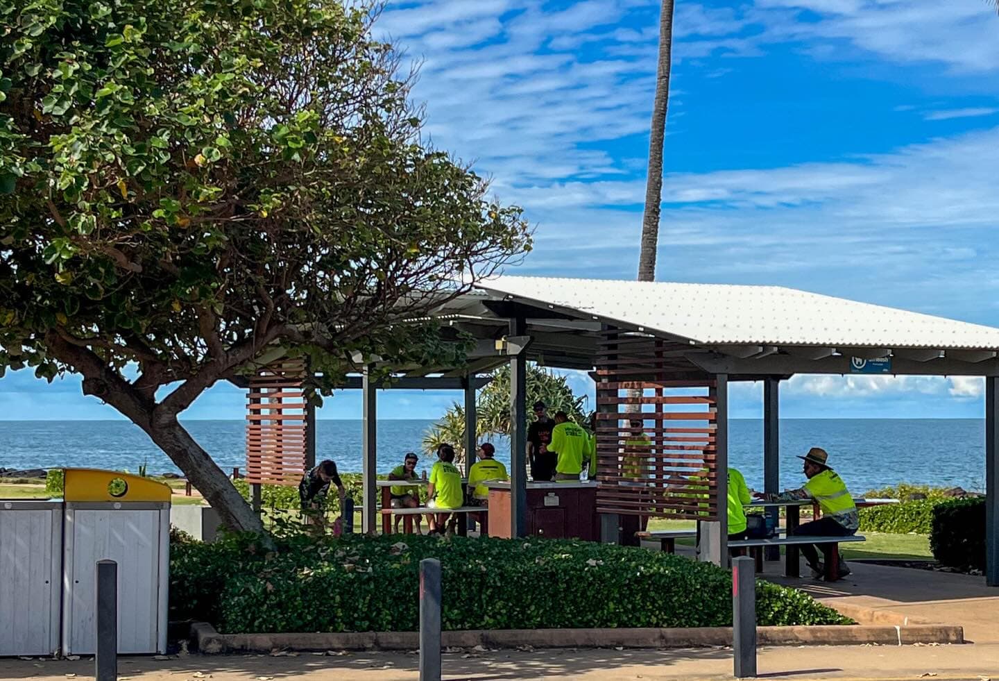 Members of the site crew taking a break at the beachfront picnic shelter on the Bargara Esplanade, the ocean directly behind them