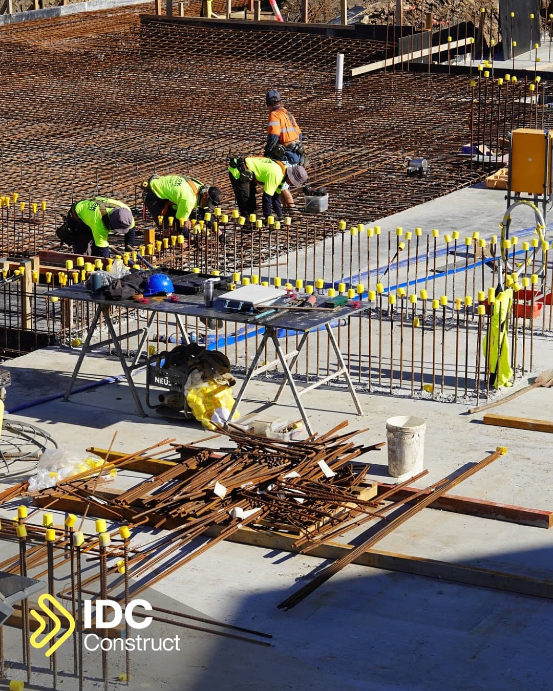 Steel fixers tying reinforcement bar across the Mira Living foundations, capped starter bars running the length of the slab